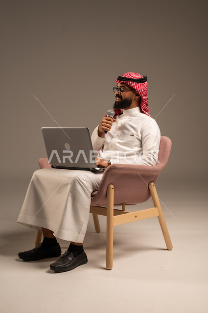 إجراء المقابلات وطرح الأسئلة، استخدام الأجهزة التقنية الحديثة، بورتريه لرجل عربي خليجي سعودي يرتدي الثوب التقليدي والشماغ يجلس على الكرسي يستخدم الحاسوب المحمول ويحمل بيده مكبر الصوت يقوم بإلقاء الخطابات، خلفية رمادية