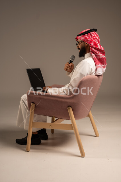 استخدام الأجهزة التقنية الحديثة، بورتريه من الجانب لرجل عربي خليجي سعودي يرتدي الثوب التقليدي والشماغ يجلس على الكرسي يستخدم الحاسوب المحمول ويحمل بيده مكبر الصوت يقوم بإلقاء الخطابات، إجراء المقابلات وطرح الأسئلة، خلفية رمادية