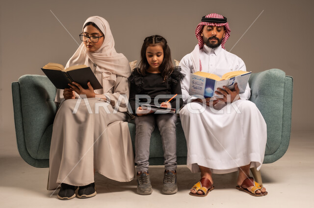 شغف المطالعة للكتب والروايات، القيام بالانشطة المسلية في المنزل، تعليم الاولاد على التثقيف والمطالعة، قضاء وقت ممتع مع الأبناء، بورتريه لرجل عربي خليجي سعودي يجلس على الكنبة  بجانب زوجته وابنته يقومون بقراءة القصص، تنمية المهارات الأدبية والفنية، خلفية رمادية