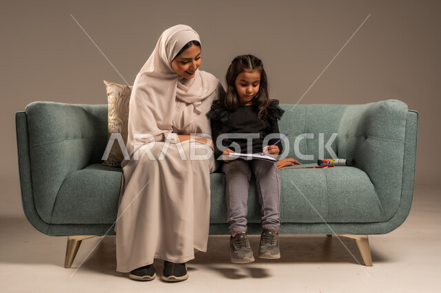 الاهتمام بتعليم الأبناء ودعمهم، بورتريه لام عربية سعودية خليجية ترتدي عباءة ملونة تجلس على كرسي مريح تقوم بتدريس ابنتها، المساعدة في تأدية الواجبات المدرسية، الانشطة التعليمية وتنمية القدرات، خلفية رمادية