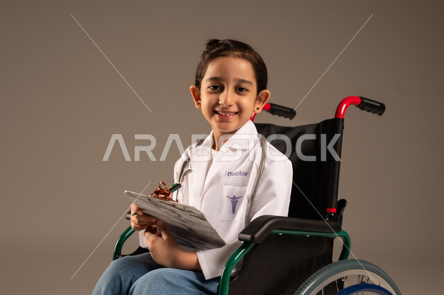 الطموحات و الأهداف المستقبلية في العمل في العيادات والمشافي، تدوين وتسجيل معلومات وبيانات المرضى، تحديد مهنة المستقبل منذ الصغر، بورتريه لفتاة عربية خليجية سعودية من ذوي الاحتياجات الخاصة ترتدي زي ممرضة تجلس على كرسي متحرك تمسك بيدها ملف ملاحظات، خلفية رمادية