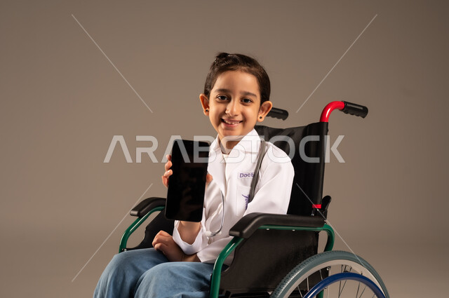 عرض شاشة سوداء فارغة عبر الهاتف المحمول، الطموحات والأهداف المستقبلية في العمل في العيادات والمشافي، استخدام الأجهزة التقنية الحديثة، بورتريه لفتاة عربية خليجية سعودية من ذوي الاحتياجات الخاصة ترتدي زي ممرضة تجلس على كرسي متحرك، خلفية رمادية