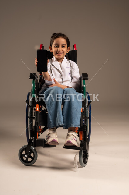 عرض شاشة سوداء فارغة عبر الهاتف المحمول، الطموحات والأهداف المستقبلية في العمل في العيادات والمشافي، استخدام الأجهزة التقنية الحديثة، بورتريه لفتاة عربية خليجية سعودية من ذوي الاحتياجات الخاصة ترتدي زي ممرضة تجلس على كرسي متحرك، خلفية رمادية