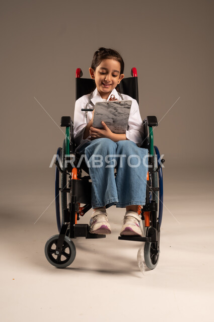 الطموحات و الأهداف المستقبلية في العمل في العيادات والمشافي، تدوين وتسجيل معلومات وبيانات المرضى، تحديد مهنة المستقبل منذ الصغر، بورتريه لفتاة عربية خليجية سعودية من ذوي الاحتياجات الخاصة ترتدي زي ممرضة تجلس على كرسي متحرك تمسك بيدها ملف ملاحظات، خلفية رمادية