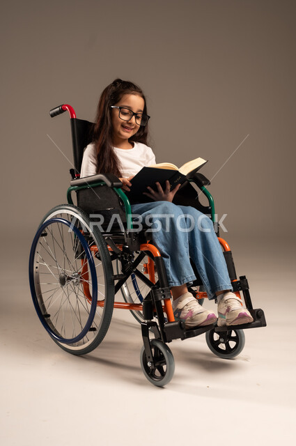 تنمية المهارات الفنية والذهنية، استغلال أوقات الفراغ بالأنشطة التعليمية، بورتريه لفتاة عربية خليجية سعودية من ذوي الاحتياجات الخاصة ترتدي الزي الكاجوال تجلس على كرسي متحرك تقوم بالمطالعة وقراءة الكتب المفيده، مراجعة الدروس اليومية، خلفية رمادية