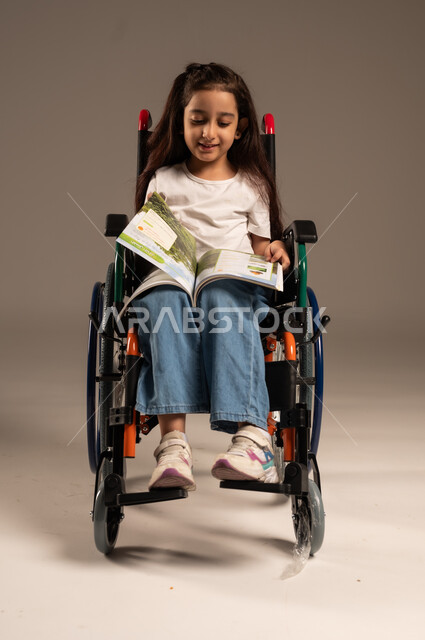 تنمية المهارات الفنية والذهنية، مراجعة الدروس اليومية، استغلال أوقات الفراغ بالأنشطة التعليمية، بورتريه لفتاة عربية خليجية سعودية من ذوي الاحتياجات الخاصة ترتدي الزي الكاجوال تجلس على كرسي متحرك تقوم بالمطالعة وقراءة الكتب المفيده، خلفية رمادية