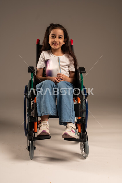  تنمية المهارات الفنية والذهنية، مراجعة الدروس اليومية، استغلال أوقات الفراغ بالأنشطة التعليمية، بورتريه لفتاة عربية خليجية سعودية من ذوي الاحتياجات الخاصة ترتدي الزي الكاجوال تجلس على كرسي متحرك تقوم بالمطالعة وقراءة الكتب المفيده، خلفية رمادية