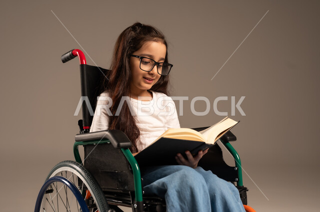 استغلال أوقات الفراغ بالأنشطة التعليمية، بورتريه لفتاة عربية خليجية سعودية من ذوي الاحتياجات الخاصة ترتدي الزي الكاجوال تجلس على كرسي متحرك تقوم بالمطالعة وقراءة الكتب المفيده،  تنمية المهارات الفنية والذهنية، مراجعة الدروس اليومية، خلفية رمادية