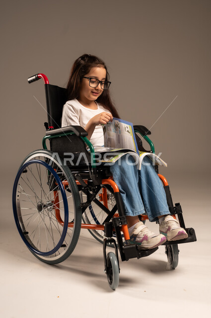 استغلال أوقات الفراغ بالأنشطة التعليمية، بورتريه لفتاة عربية خليجية سعودية من ذوي الاحتياجات الخاصة ترتدي الزي الكاجوال تجلس على كرسي متحرك تقوم بالمطالعة وقراءة الكتب المفيده،  تنمية المهارات الفنية والذهنية، مراجعة الدروس اليومية، خلفية رمادية