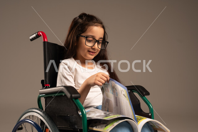 استغلال أوقات الفراغ بالأنشطة التعليمية، بورتريه لفتاة عربية خليجية سعودية من ذوي الاحتياجات الخاصة ترتدي الزي الكاجوال تجلس على كرسي متحرك تقوم بالمطالعة وقراءة الكتب المفيده،  تنمية المهارات الفنية والذهنية، مراجعة الدروس اليومية، خلفية رمادية