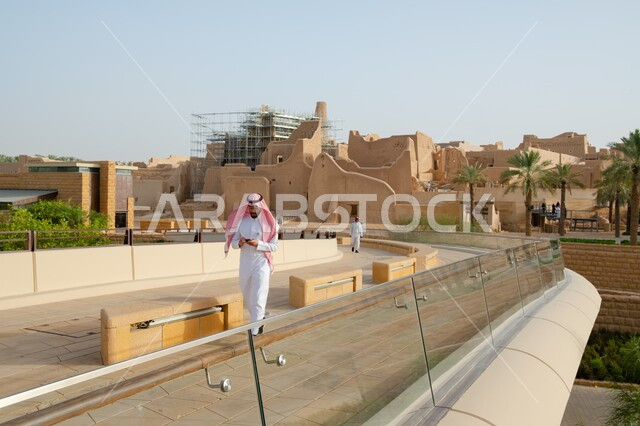 أماكن السياحة التراثية في السعودية، ذكرى تأسيس الدولة السعودية الأولى في ٢٢ فبراير، أسوار قصر سلوى في الدرعية القديمة، المباني والبيوت الأثرية الطينية، رجل عربي خليجي سعودي يرتدي الثوب التقليدي والشماغ يمسك بيده الهاتف المحمول، التجول في القرى والأحياء السكنية الشعبية