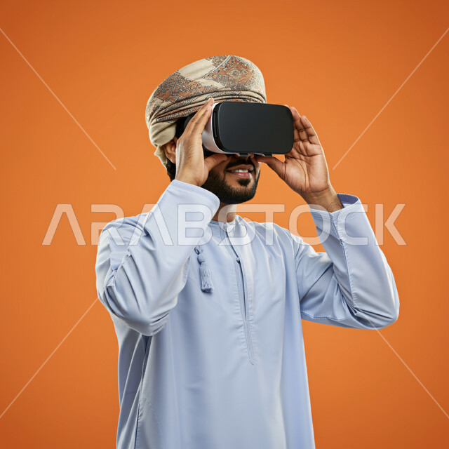 Integration and simulation of the imaginary world, technical and technological development, fun and entertainment by watching through virtual reality glasses, close-up portrait of a young Gulf Arab Omani man wearing a dishdasha and turban looking through 3D glasses and holding them in his hand, orange background