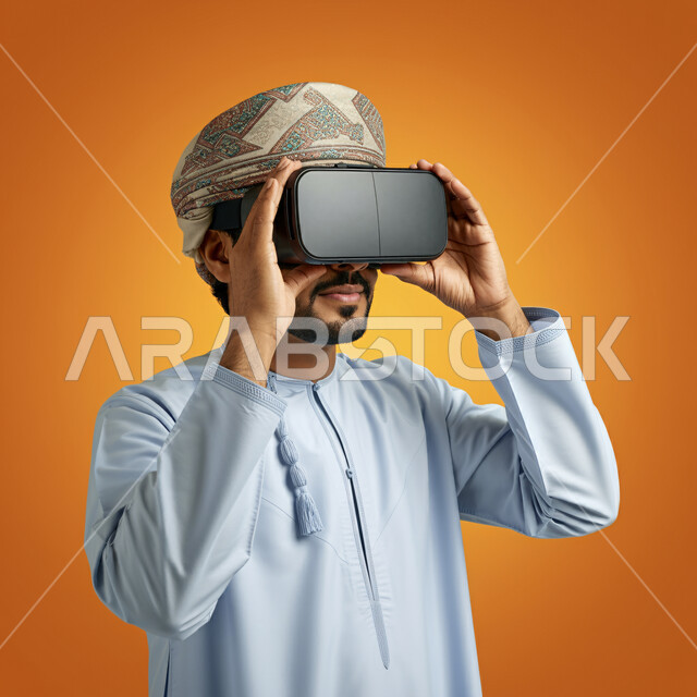 Technical and technological development, fun and entertainment by watching through virtual reality glasses, close-up portrait of a young Gulf Arab Omani man wearing a dishdasha and turban looking through 3D glasses and holding them in his hand, integration and simulation of the imaginary world, orange background
