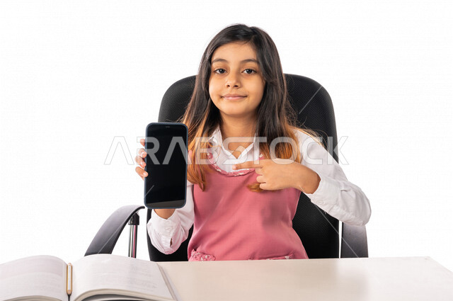 تلميذة عربية خليجية سعودية ترتدي الزي المدرسي ، تستخدم الهاتف المحمول  ، التعليم الالكتروني ، الدراسة عن بعد،  متابعة الدروس والواجبات عبر الانترنت ،فصل دراسي جديد، التعليم في المملكة العربية السعودية ، خلفية بيضاء