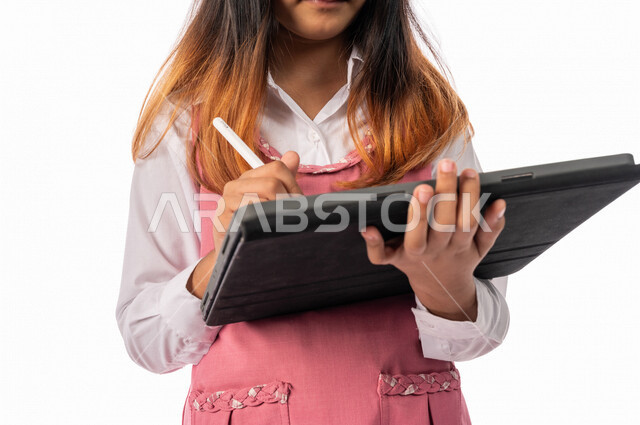A Saudi Arabian Gulf schoolgirl wearing a school uniform, using a tablet, e-learning, distance study, following up on lessons and assignments online, new semester, education in Saudi Arabia, white background