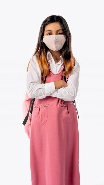 تلميذة عربية خليجية سعودية ترتدي الزي المدرسي والحقيبة المدرسية ،ترتدي الكمامة للوقاية من فايروس كورونا ، الاستعداد للفصل الدراسي الجديد، التعليم في المملكة العربية السعودية ، خلفية بيضاء