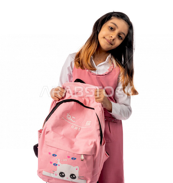 تصوير من الامام لتلميذة عربية خليجية سعودية ترتدي الزي المدرسي وبيدها الحقيبة المدرسية  ،مستعدة للذهاب الى المدرسة ، الاستعداد للفصل الدراسي الجديد، التعليم في المملكة العربية السعودية ، خلفية بيضاء