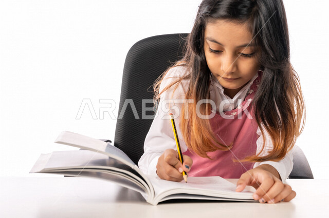 تلميذة عربية خليجية سعودية ترتدي الزي المدرسي ، مستمتعة بقراءة الكتاب الدراسي ، حل الواجبات المدرسية ،فصل دراسي جديد، التعليم في المملكة العربية السعودية ، خلفية بيضاء