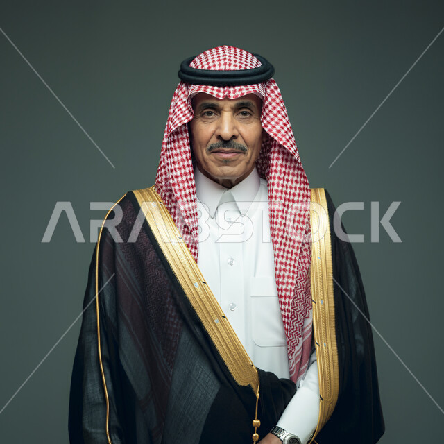 مفهوم الرجولة والقوة والثقة في النفس، الأزياء التراثية العصرية، الاهتمام بالأناقة والمظهر الخارجي، بورتريه مقرب لرجل عربي خليجي سعودي مبتسم يرتدي الشماغ والبشت التقليدي الأسود ينظر إلى الكاميرا بإيماءات الجدية والفخر، خلفية رمادية