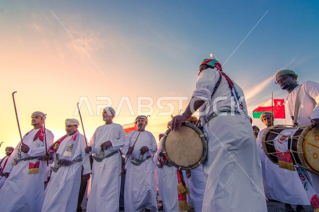 المشاركة بالاعياد والمناسبات الوطنية، الاحتفال بذكرى اليوم الوطني العماني، الاعتزاز والفخر بالرموز والراية العمانية، مجموعة من الرجال العرب الخليجيين العمانين يقومون بالاحتفال والاندماج مع الرقص الشعبي والاهازيج، مفهوم حب الوطن والإنتماء إليه، ارتداء أزياء العرضه النجدية الشعبية