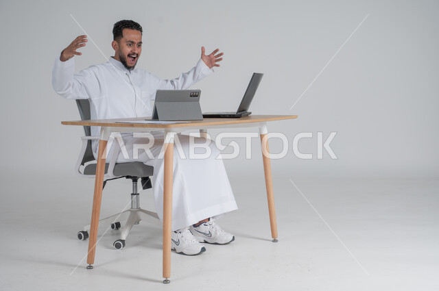 Using modern and advanced technologies, making a video call via tablet, portrait of a young Saudi Arabian Gulf man wearing traditional thobe, wearing headphones and working remotely using a laptop, gestures of anger and nervousness, Saudi work environment, white background