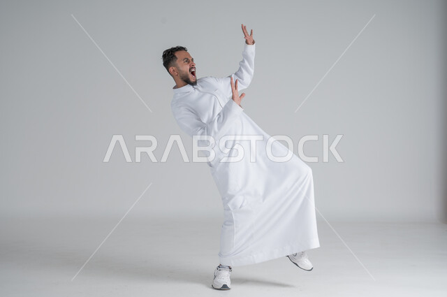 رفع اليدين عاليا بتعابير الصراخ الشديد، ايماءات الاستهبال والسخريه، بورتريه لشاب عربي خليجي سعودي يرتدي الثوب التقليدي على وشك السقوط على الارض، الجسم بالطول الكامل، خلفية بيضاء