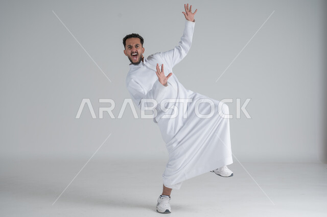 رفع اليدين عاليا بتعابير الصراخ الشديد، ايماءات الاستهبال والسخريه، بورتريه لشاب عربي خليجي سعودي يرتدي الثوب التقليدي على وشك السقوط على الارض، الجسم بالطول الكامل، خلفية بيضاء