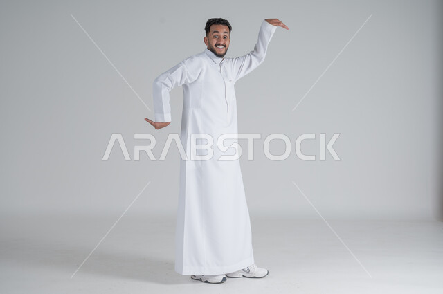ايماءات الاستهبال والسخريه، بورتريه لرجل عربي سعودي خليجي يرتدي الثوب التقليدي يرفع يديه بتعابير الرقص, الجسم بالطول الكامل, خلفية بيضاء