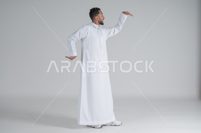 ايماءات الاستهبال والسخريه، بورتريه لرجل عربي سعودي خليجي يرتدي الثوب التقليدي يرفع يديه بتعابير الرقص, الجسم بالطول الكامل, خلفية بيضاء