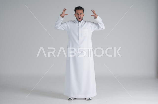 رفع اليدين عاليا بتعابير الصراخ الشديد، ايماءات الغضب والانزعاج، بورتريه لشاب عربي خليجي سعودي يرتدي الثوب التقليدي يرفع كفيه بتذمر، الجسم بالطول الكامل، خلفية بيضاء