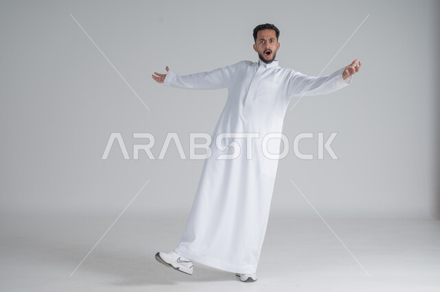 رفع اليدين عاليا بتعابير الصراخ الشديد، ايماءات الاستهبال والسخريه، بورتريه لشاب عربي خليجي سعودي يرتدي الثوب التقليدي على وشك السقوط على الارض، الجسم بالطول الكامل، خلفية بيضاء