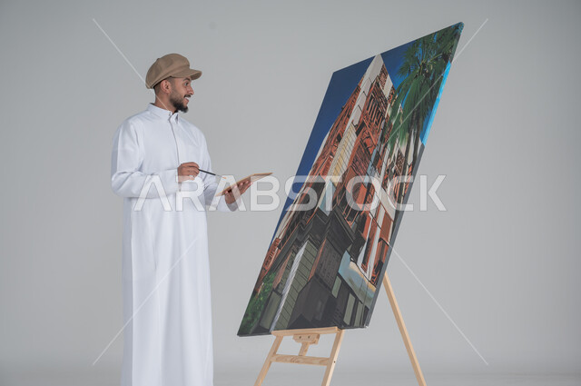 استخدام ريشة التلوين، أنشطة ترفيهية فنية ممتعة، بورتريه مقرب لرسام عربي خليجي سعودي يرتدي الثوب التقليدي وقبعة يحمل بيديه  الالوان المائية, ورشة عمل وفنون,  خلفية بيضاء