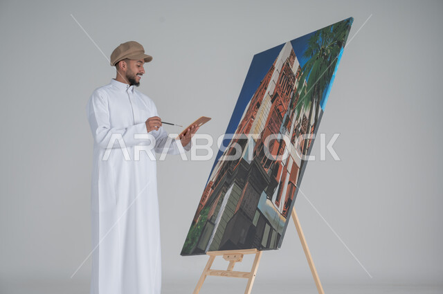 استخدام ريشة التلوين، أنشطة ترفيهية فنية ممتعة، بورتريه مقرب لرسام عربي خليجي سعودي يرتدي الثوب التقليدي وقبعة يحمل بيديه  الالوان المائية, ورشة عمل وفنون,  خلفية بيضاء