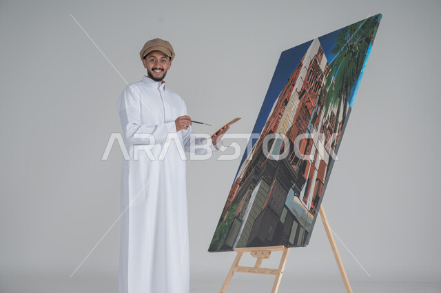 استخدام ريشة التلوين، أنشطة ترفيهية فنية ممتعة، بورتريه مقرب لرسام عربي خليجي سعودي يرتدي الثوب التقليدي وقبعة يحمل بيديه  الالوان المائية, ورشة عمل وفنون,  خلفية بيضاء