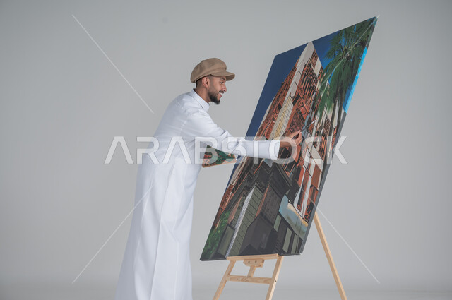 استخدام ريشة التلوين، أنشطة ترفيهية فنية ممتعة، بورتريه مقرب لرسام عربي خليجي سعودي يرتدي الثوب التقليدي وقبعة يحمل بيديه  الالوان المائية, ورشة عمل وفنون,  خلفية بيضاء