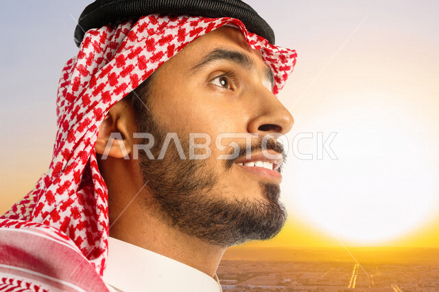 Close-up side view of stylish smiling Saudi Arabian Gulf Arab man, looking up, with sunset and sunrise background