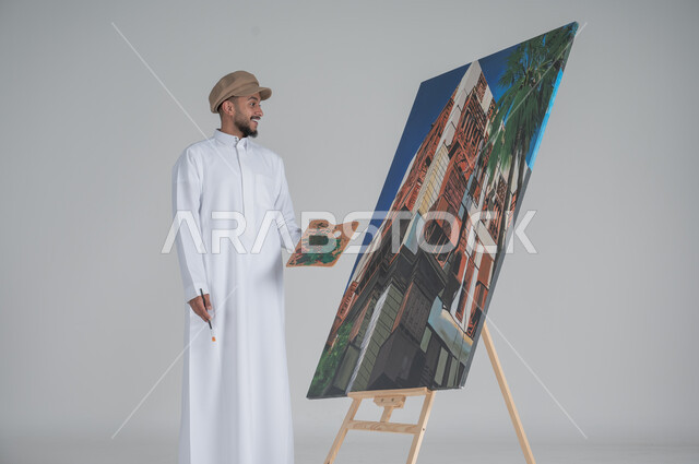 استخدام ريشة التلوين، أنشطة ترفيهية فنية ممتعة، بورتريه مقرب لرسام عربي خليجي سعودي يرتدي الثوب التقليدي وقبعة يحمل بيديه  الالوان المائية, ورشة عمل وفنون,  خلفية بيضاء