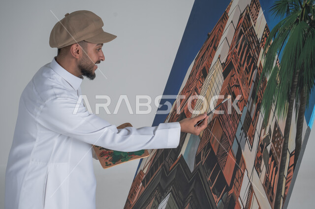 استخدام ريشة التلوين، أنشطة ترفيهية فنية ممتعة، بورتريه مقرب لرسام عربي خليجي سعودي يرتدي الثوب التقليدي وقبعة يحمل بيديه  الالوان المائية, ورشة عمل وفنون,  خلفية بيضاء
