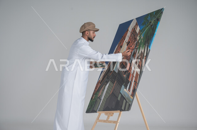 ورشة عمل وفنون, استخدام ريشة التلوين، أنشطة ترفيهية فنية ممتعة، بورتريه مقرب لرسام عربي خليجي سعودي يرتدي الثوب التقليدي وقبعة يحمل بيديه  الالوان المائية, خلفية بيضاء