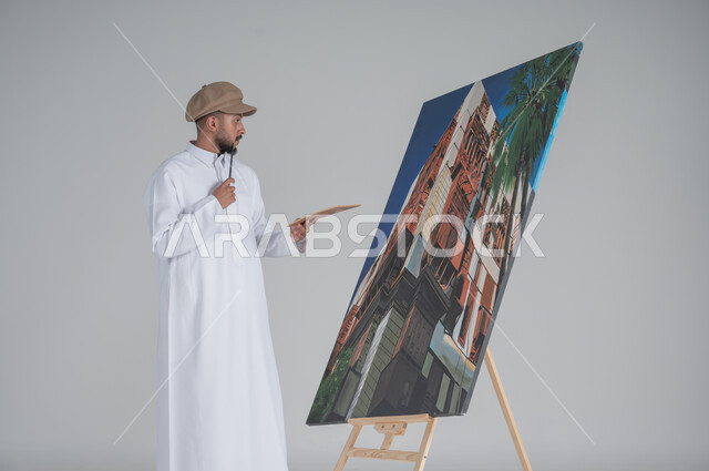 ورشة عمل وفنون, استخدام ريشة التلوين، أنشطة ترفيهية فنية ممتعة، بورتريه مقرب لرسام عربي خليجي سعودي يرتدي الثوب التقليدي وقبعة يحمل بيديه  الالوان المائية, خلفية بيضاء