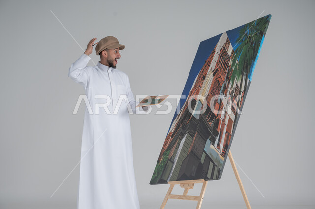 النظر الى اللوحة بايماءات الصدمة والذهول, ورشة عمل وفنون, استخدام ريشة التلوين، أنشطة ترفيهية فنية ممتعة، بورتريه لرسام عربي خليجي سعودي يرتدي الثوب التقليدي وقبعة يحمل بيديه  الالوان المائية,  خلفية بيضاء