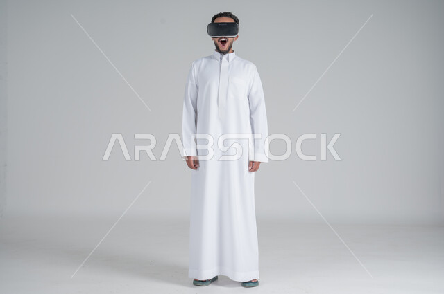 Technological and technical development, portrait of a Saudi Gulf Arab man wearing a traditional thobe and 3D virtual reality glasses, merging modern technologies with fun and entertainment, gestures of integration and concentration, full-length body image, white background