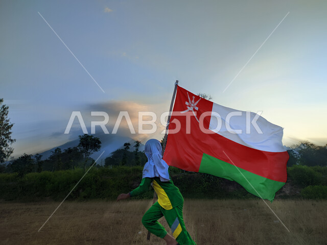 المشاركة بالأعياد والمناسبات الوطنية،, حب الوطن والانتماء إليه، ولد عربي خليجي عماني يحمل بيده علم سلطنة عمان، الاحتفال بذكرى اليوم الوطني العماني 18 نوفمبر،  إحياء ذكرى تأسيس الدولة 1775 م، الركوض في احدى المناطق العمانية، الاعتزاز والفخر بالرموز والراية