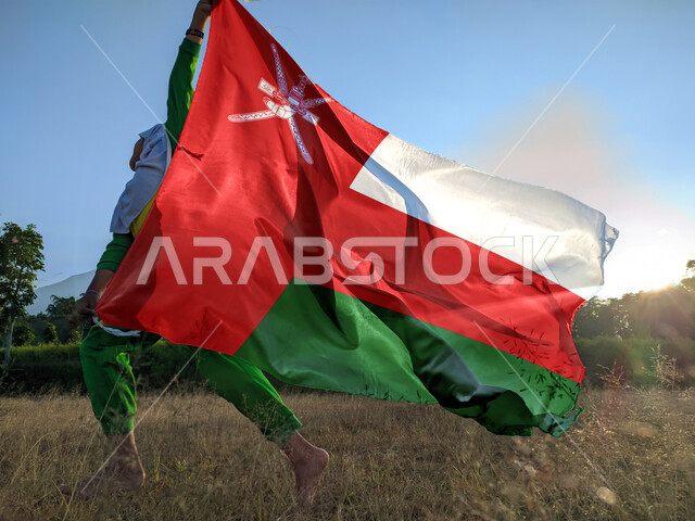 المشاركة بالأعياد والمناسبات الوطنية،, حب الوطن والانتماء إليه، ولد عربي خليجي عماني يحمل بيده علم سلطنة عمان، الاحتفال بذكرى اليوم الوطني العماني 18 نوفمبر،  إحياء ذكرى تأسيس الدولة 1775 م، الركوض في احدى المناطق العمانية، الاعتزاز والفخر بالرموز والراية