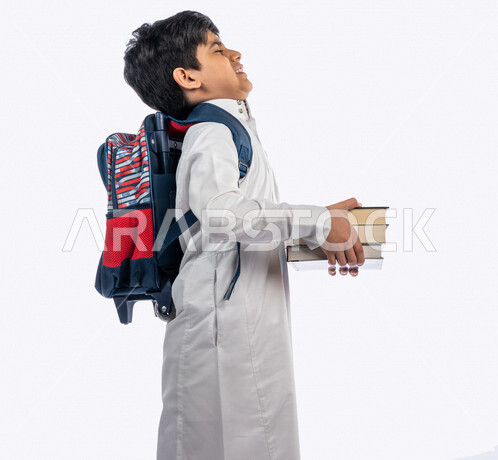 Portrait of a Saudi Arabian Gulf school student, wearing a school backpack, and wearing the traditional Saudi thobe, holding in his hand a group of textbooks, gestures and facial expressions and hands indicating fatigue, new school year, Saudi school