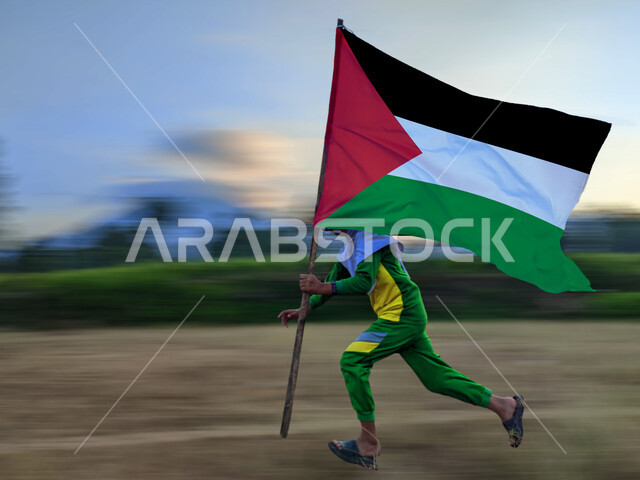 Remembrance of the celebration of the Palestinian National Day, November 15, the day we began in 1988 AD, love of the homeland and belonging to it, a Palestinian Arab boy raising the flag of the Palestinian state in his hand, participation in worship and national occasions, running in one of the areas of the country