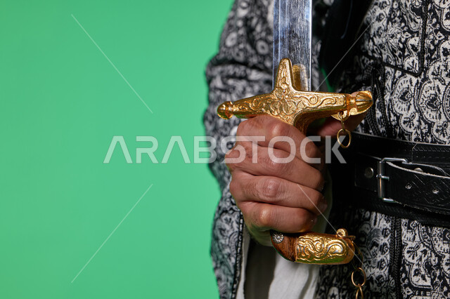 ذكرى يوم التأسيس، صورة مقربة ليد رجل عربي خليجي سعودي يرتدي زي تراثي سعودي للمناسبات الوطنية والاحتفالية ويمسك السيف، تاسيس الدولة السعودية الاولى 1727م، زي سعودي شعبي، كروما، خلفية خضراء
