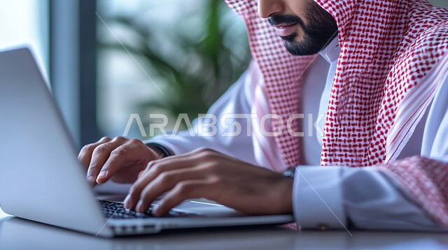 وظائف ومهن مكتبية سعودية، دمج العمل مع التكنولوجيا, إنجاز المهام المطلوبة، إدارة شؤون الشركة وتنظيمها عبر الاجهزة التقنية، صورة مقربة لرجل عربي خليجي سعودي يرتدي الزي التقليدي والشماغ يعمل على الحاسوب المحمول