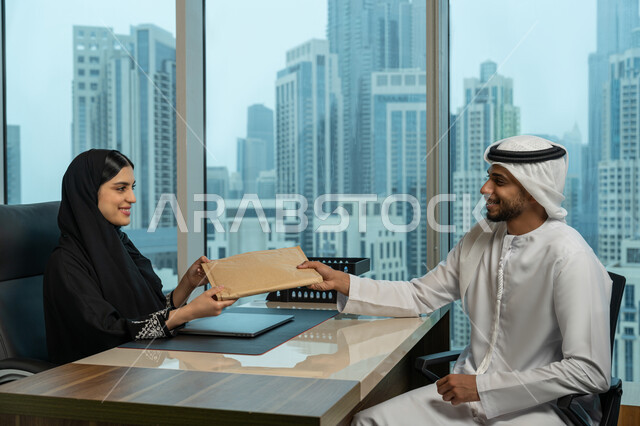 مهن ووظائف نسائية مكتبية، نقل وتسجيل البيانات، صورة مقربة لرجل عربي خليجي اماراتي يرتدي الكندورة والغترة يقوم بتمرير الوثائق للموظفة، بيئة العمل المريحة في شركات الامارات