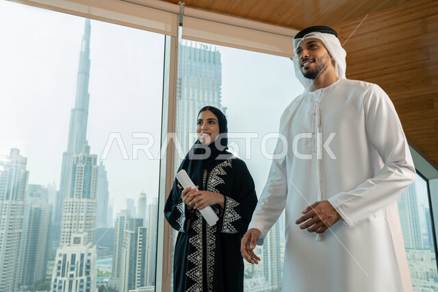 بيئة العمل المريحة في شركات الامارات، اجتماعات وورشات عمل في مقر الشركة، تطوير ودراسة المشاريع الجديدة، جمع البيانات وحل المشكلات، امرأة عربية خليجية اماراتية محجبة ترتدي العباءة تحمل بيدها مجموعة من الاوراق تقوم بمناقشة المشروع مع زميلها